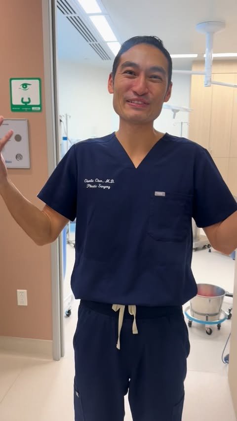 Dr. Charlie Chen smiling in navy 'Charlie Chen, M.D. Plastic Surgery' scrubs inside his accredited surgery center