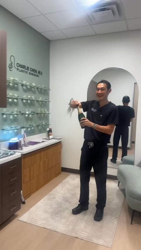 Dr. Chen smiling as he pops a bottle of champagne inside the new office, celebrating the grand opening