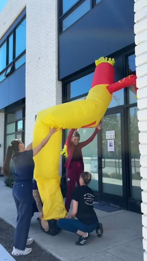 Staff members playfully wrangling a yellow inflatable tube man outside the office while preparing for the grand opening